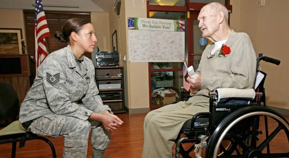 Elderly man sitting in a wheelchair talking to a young female soldier