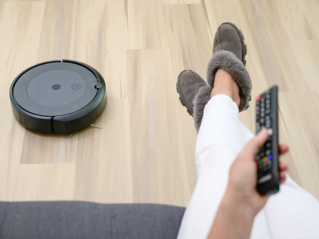 Woman holding a remote while a roomba cleans the floor beneath her