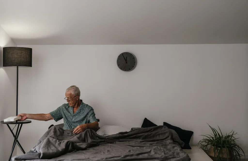 Elderly man sitting in bed putting something down on desk