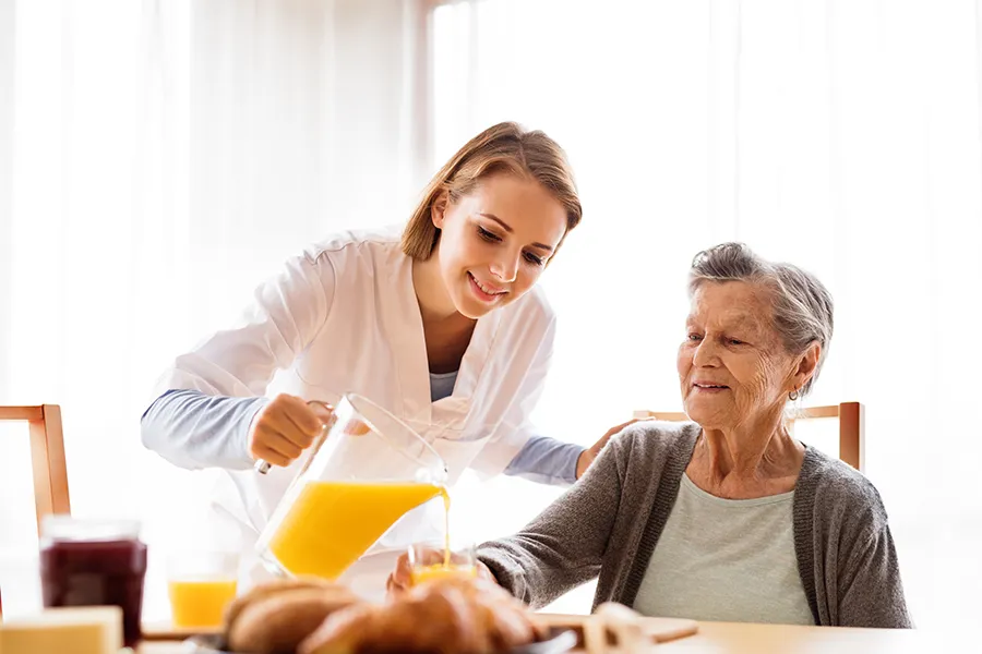 home care pricing - female caregiver assisting elderly woman with pouring orange juice